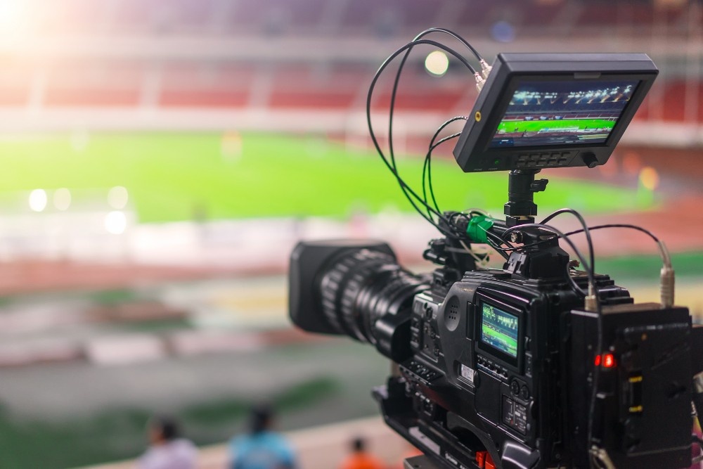 Professional video camera setup at a stadium, with a blurred-out football field in the background, representing a Business Videos Agency in Park Pointe