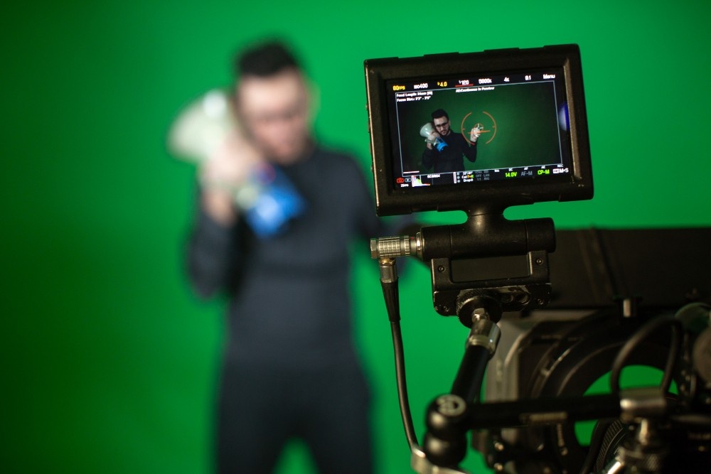 A video monitor shows a man holding a product in front of a green screen, representing professional post-production and visual effects services from a Business Videos Production company in Sugar Land