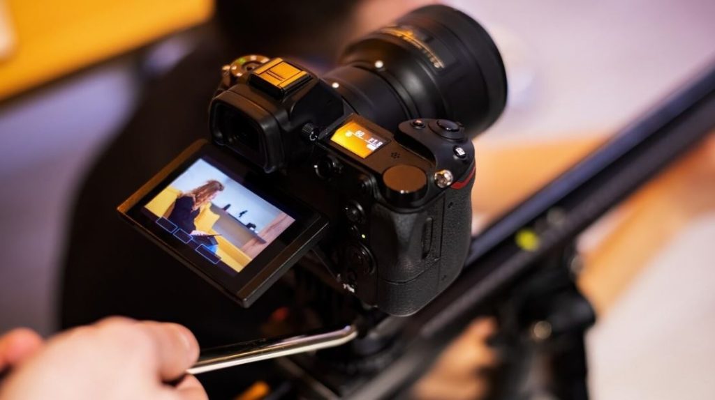 A close-up of a professional video camera on a tripod, with its flip-out screen showing a person being filmed, representing the services of a Corporate Video Production Company in Woodbridge