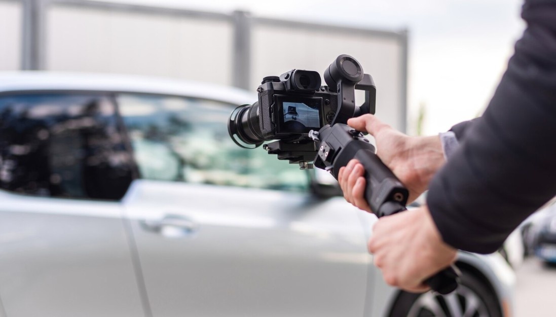 Person holding a video camera on a gimbal stabilizer, filming a car to create a commercial for a Business Videos Agency in Covington West