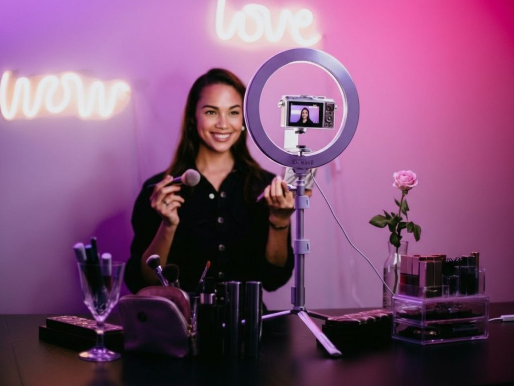 Skilled corporate video production agency in Sugar Land featuring a makeup artist using a ring light for high-quality beauty video shoots in a vibrant studio.
