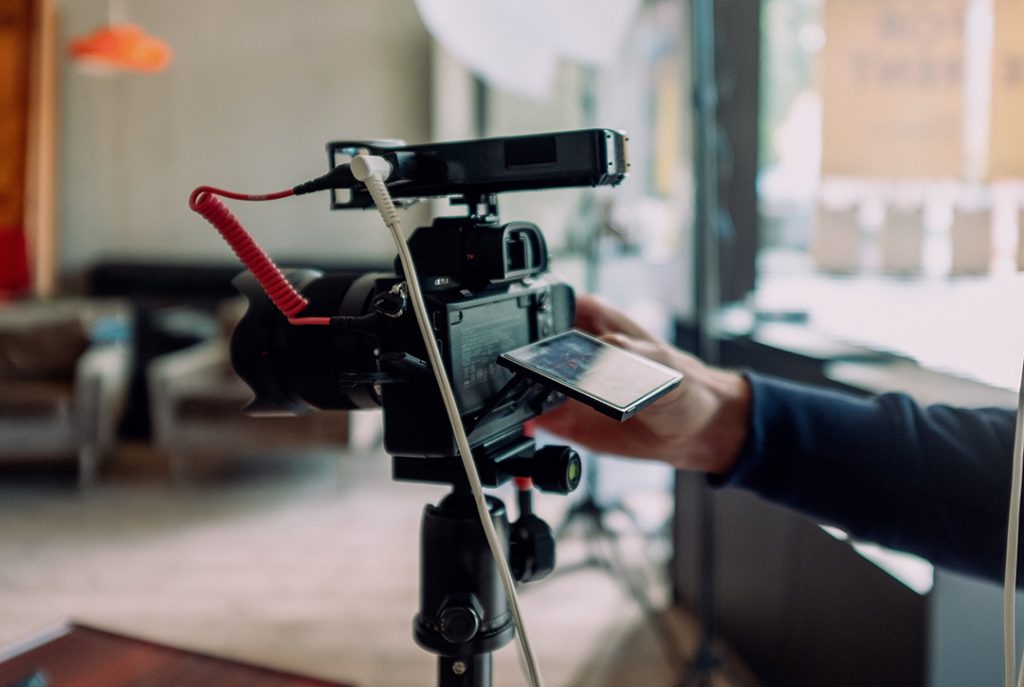 Filmmaker adjusting a camera on a tripod indoors, ready for professional corporate video production company sugar land businesses.