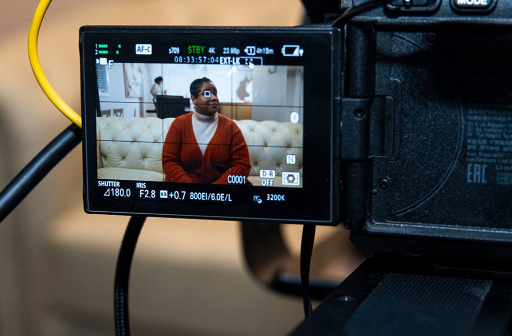 Professional camera screen with exposure settings, filming a woman on a couch for a commercial video production company Sugar Land.