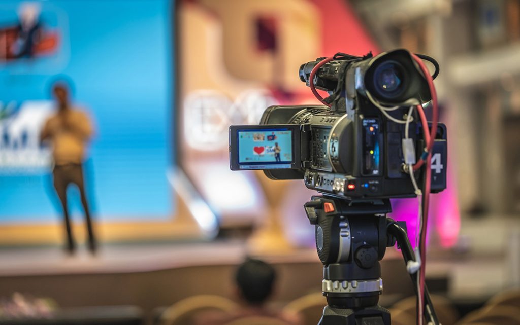 Promotional videos company sugar land capturing a speaker on stage at a corporate event with a professional video camera.