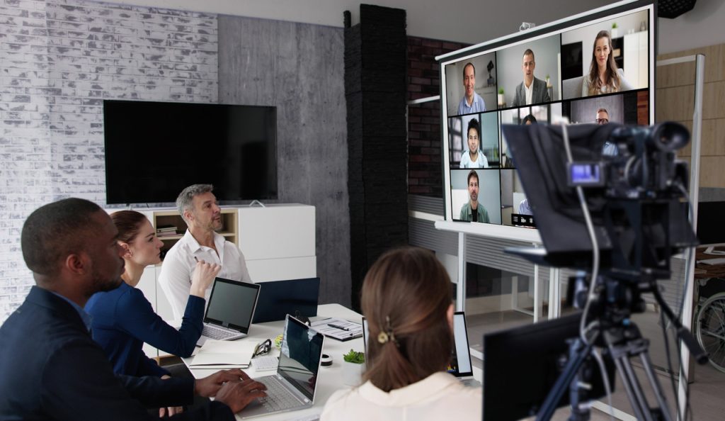 Hybrid meeting filmed by a corporate video production agency Sugar Land, featuring a remote team on a large screen.