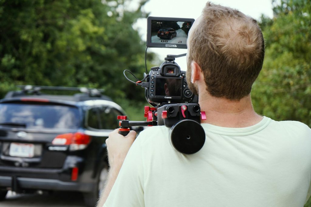 Expert camera operator using a shoulder rig for business videos production Sugar Land while tracking a moving car.