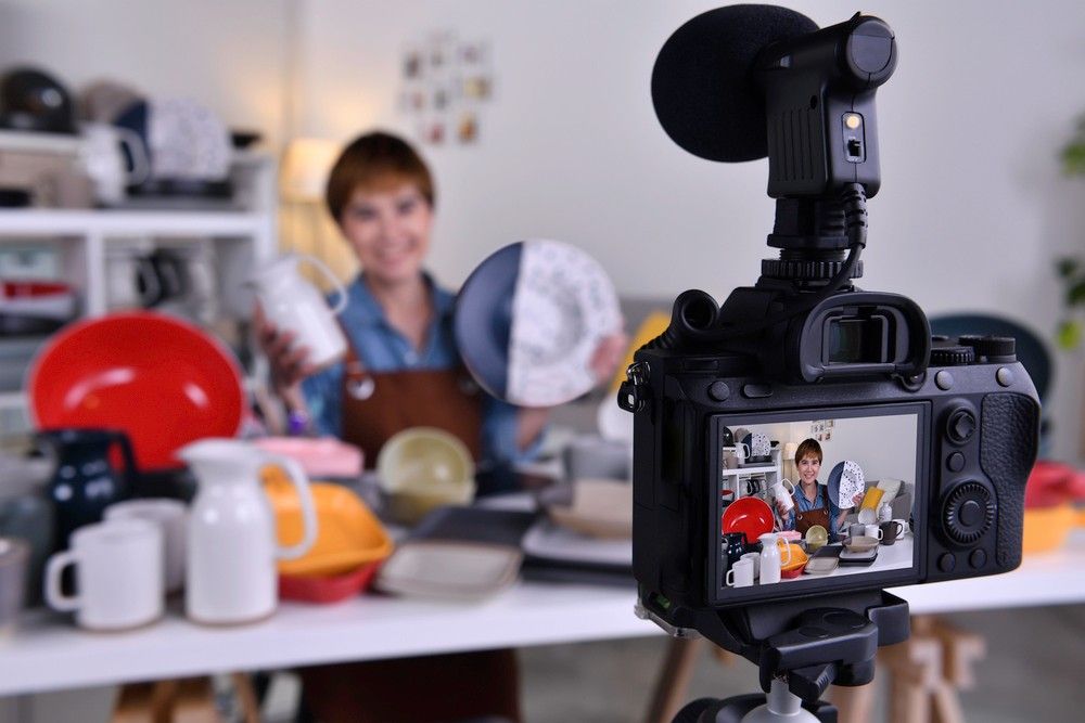 Camera on a tripod filming a woman reviewing ceramic products, showing corporate video production sugar land.