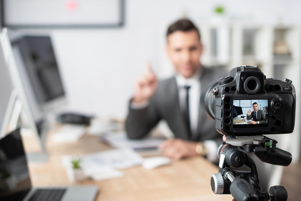 A camera on a tripod films a corporate professional in a suit for a high-traffic project by a commercial video production company in Sugar Land.