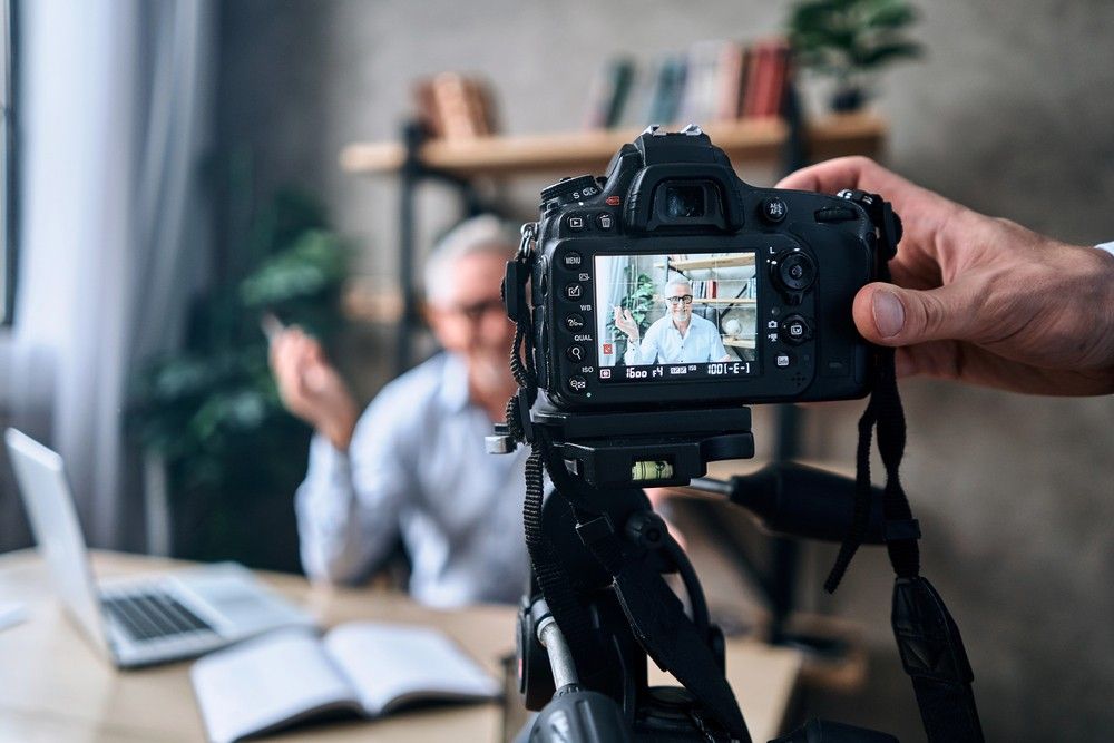 A camera on a tripod films an experienced executive for a project by a commercial video production company in Sugar Land.