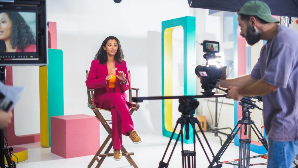 Videography company Sugar Land production crew filming a woman in a pink suit on a professional studio set with full gear.