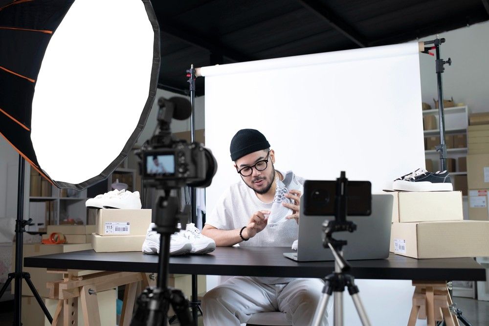 A man in a pro studio reviews sneakers, a camera on a tripod recording him for corporate video production sugar land.