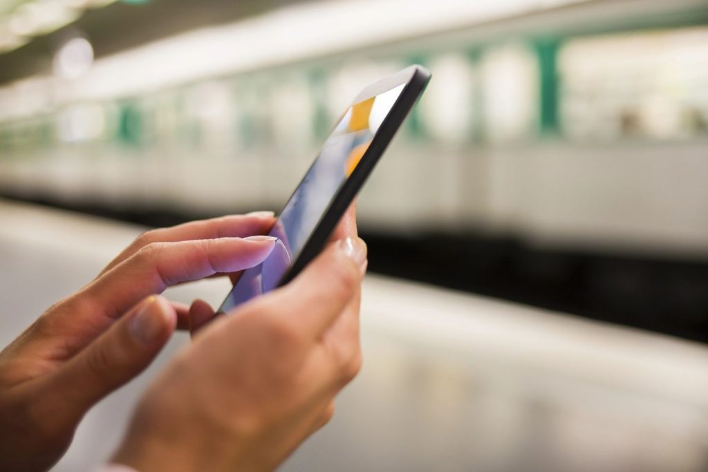 Person using a smartphone for commercial video production Sugar Land while waiting for a train at a subway station.